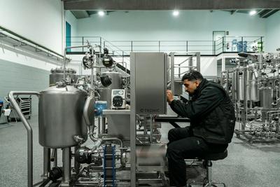 Técnico sentado a intervir numa máquina industrial de inox, numa nave de produção