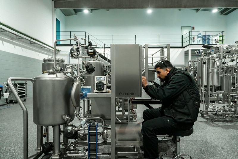 Técnico sentado a intervir numa máquina industrial de inox, numa nave de produção