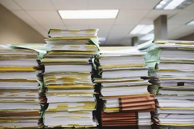 Pilhas de documentos e pastas de papel empilhadas numa secretária de escritório
