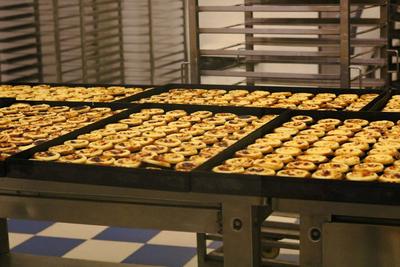 Tabuleiros de pastéis de nata numa linha de produção de pastelaria