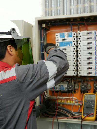 Eletricista de capacete a testar um quadro elétrico industrial aberto, com multímetro à mão