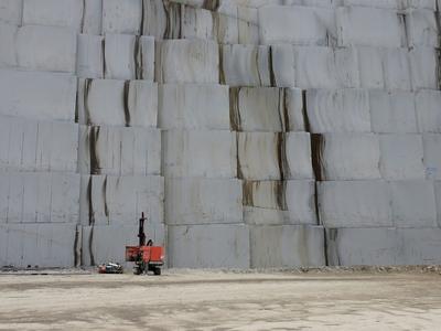 Frente de pedreira de mármore com blocos cortados e um operário à escala