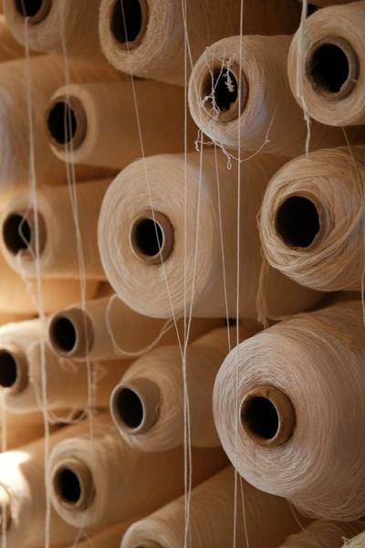 Bobinas de fio branco alinhadas numa estante de fábrica têxtil
