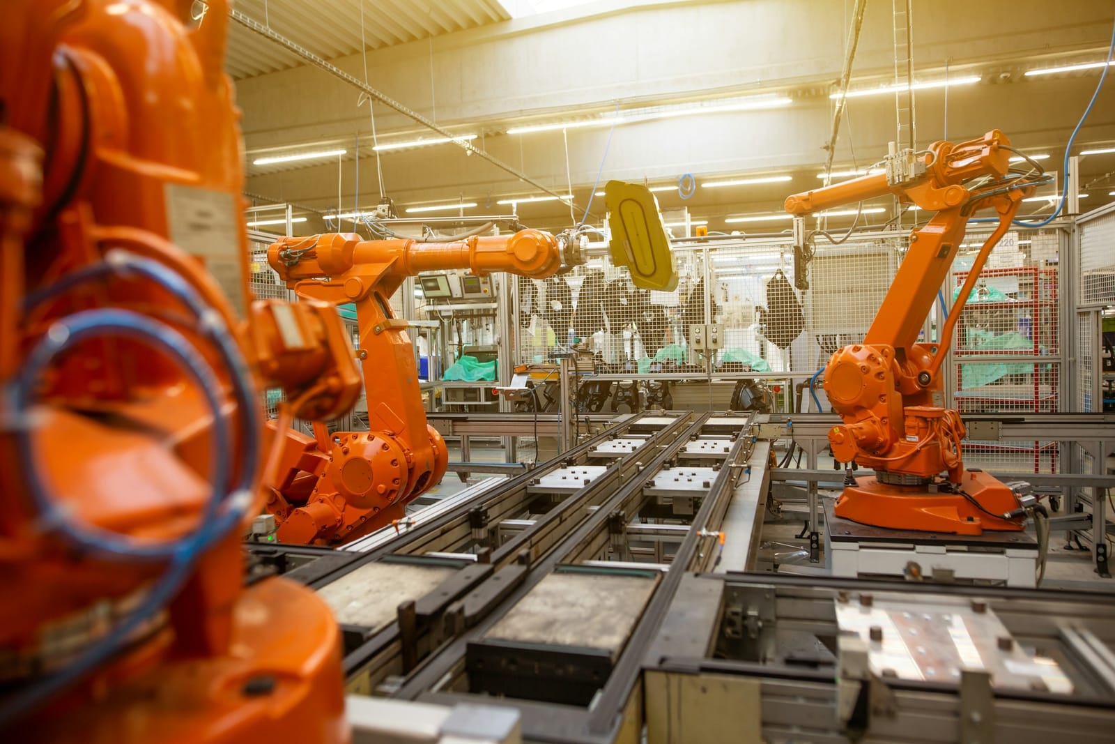 Braços robóticos laranja sobre uma linha de produção automatizada