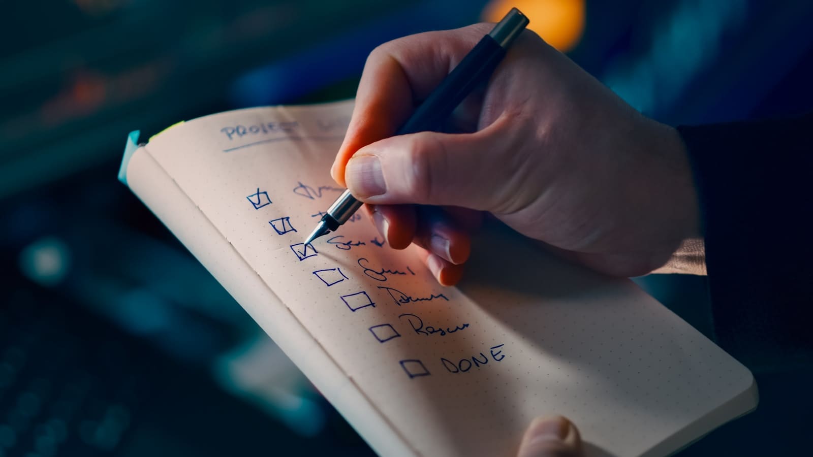 Mão a riscar itens concluídos numa lista de verificação de projeto, num caderno