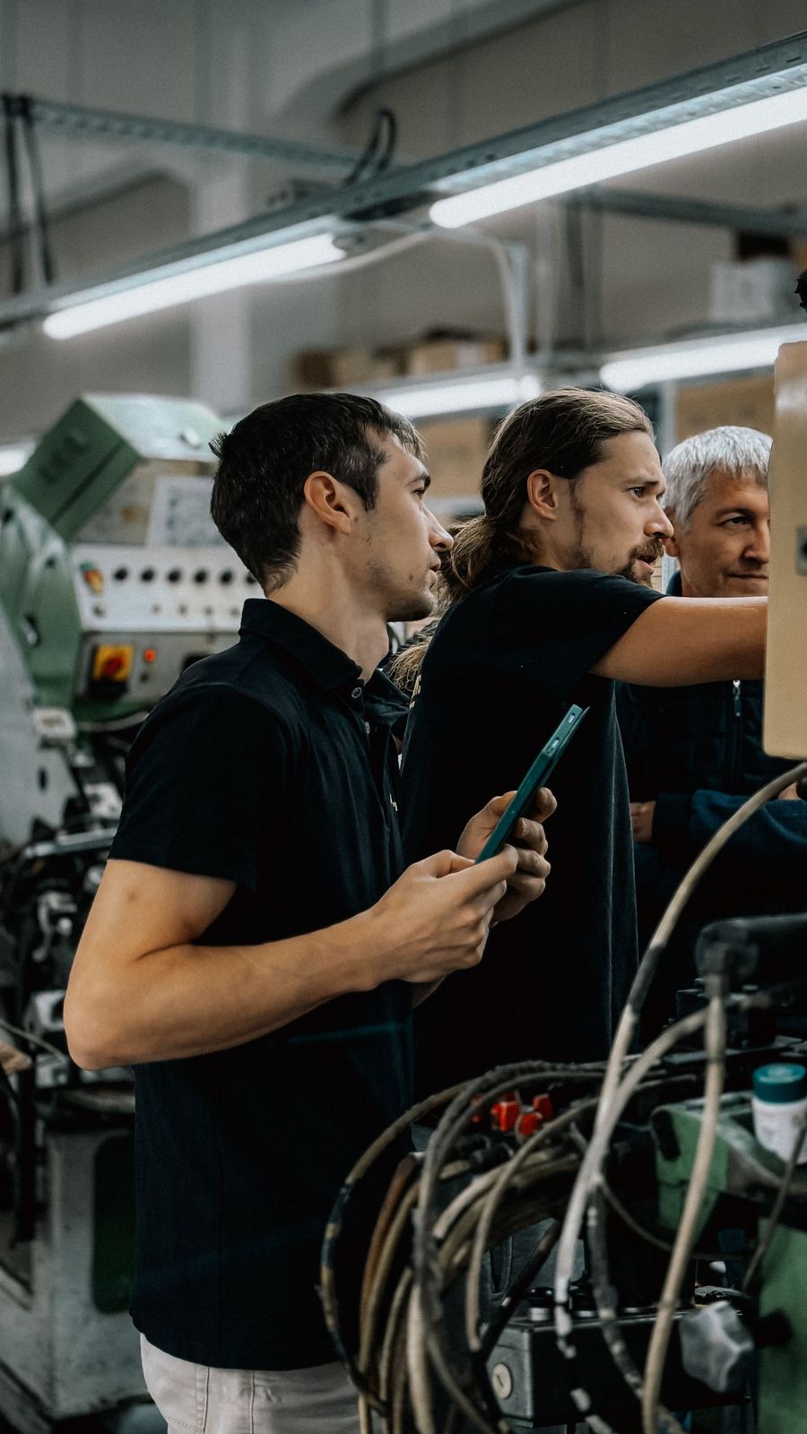 Três técnicos junto a uma máquina numa oficina, a discutir uma afinação com um tablet na mão